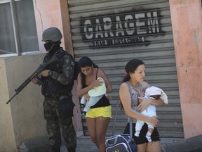 In this Tuesday, Oct. 10, 2017 photo, women cradle their babies as they walk past a soldier during an operation at the Rocinha slum, in Rio de Janeiro, Brazil. More than 1,000 Brazilian police and soldiers are searching Rio's largest slum for weapons and ammunition amid a crackdown on drug gangs. In recent weeks, a series of intense shootouts led Brazilian authorities to ask the military for help patrolling the perimeter of Rocinha. (AP Photo/Silvia Izquierdo)