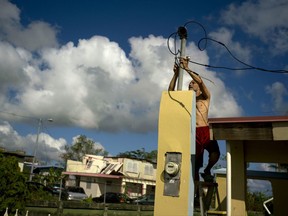 In this Friday, Oct. 13, 2017 photo, a resident tries to connect electrical lines downed by Hurricane Maria in preparation for when electricity is restored in Toa Baja, Puerto Rico. A month after the storm rolled across the center of Puerto Rico, power is still out for the vast majority. (AP Photo/Ramon Espinosa)