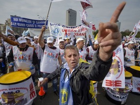 A man gestures backdropped by public sector workers hitting drums during a protest outside the government headquarters, in Bucharest, Romania, Wednesday, Oct. 4, 2017. Thousands of Romanian public sector workers rally outside the government offices to demand the government scraps plans to hike taxes paid by employees. (AP Photo/Andreea Alexandru)