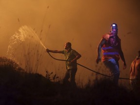 Volunteers use a water hose to fight a wild fire raging near houses in the outskirts of Obidos, Portugal, in the early hours of Monday, Oct. 16 2017. At least six people were killed Sunday as hundreds of forest fires spread across Portugal fueled by high temperatures, strong winds and a persistent drought. (AP Photo/Armando Franca)