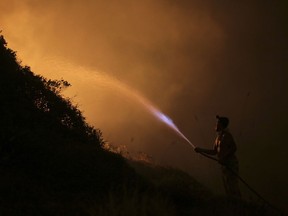 A volunteers uses a water hose to fight a wild fire raging near houses in the outskirts of Obidos, Portugal, in the early hours of Monday, Oct. 16 2017. Wildfires in Portugal killed at least 27 people, injured dozens more and left an unconfirmed number of missing in the country's second such tragedy in four months, officials said Monday. (AP Photo/Armando Franca)