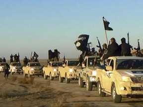 Militants of the Islamic State group hold up their weapons and wave its flags on their vehicles in a convoy to Iraq, in Raqqa, Syria in an undated photo