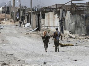 FILE - In this July 26, 2017 file photo, U.S.-backed Syrian Democratic Forces fighters walk past destroyed shops where they fight against Islamic State group militants, on the eastern side of Raqqa, Syria. As U.S.-allied fighters hurtle down the eastern banks of the Euphrates River, a showdown could ensue between the U.S. and Russia, whose allies are racing to take over the same strategic oil-rich territory from IS. (AP Photo/Hussein Malla, File)