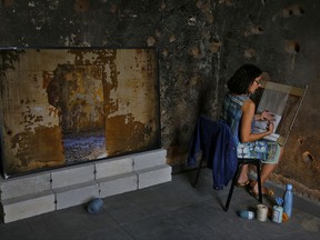 In this Saturday, Oct. 21, 2017 photo, a visitor weaves woolen patches on a loom to cover bullet holes on the building hosting an exhibition dedicated to healing the country's war wounds, in Beirut, Lebanon. Zena El Khalil's art exhibit has tapped into wounds more than forty years old in war-scarred Lebanon. "Sacred Catastrophe: Healing Lebanon" is being hosted in a landmark building in the center of Beirut, a reminder of the country's 1975-1990 civil war. (AP Photo/Bilal Hussein)