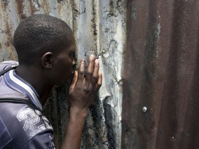 A passer by inspects damage through a hole in a fence of shops damaged by fire during clashes in the slum of Kawangware in Nairobi, Kenya, Saturday, Oct. 28, 2017. Kenyan opposition areas were calmer Saturday, a day after the country's election commission postponed voting in four restive counties where deadly clashes between police and protesters have occurred. (AP Photo/Darko Bandic)