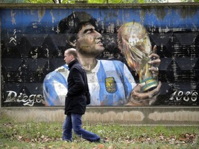 A man walks past a fence with graffiti depicting Argentina's soccer legend Diego Maradona in the town of Volkhov, 130 km (80 miles) east of St.Petersburg, Russia, Monday, Oct. 2, 2017. (AP Photo/Dmitri Lovetsky)