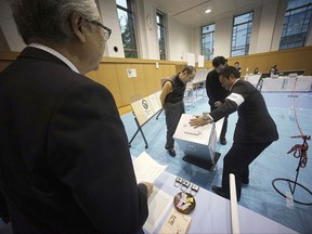 A representative of a local election administration commission shows the earliest two voters the empty ballot box before they cast their votes for a general election at a polling station in Tokyo Sunday, Oct. 22, 2017. Voting has kicked off for Japan's general election on Sunday that would most likely hand Prime Minister Shinzo Abe's ruling coalition a win, possibly retaining two-thirds in the parliament. (AP Photo/Eugene Hoshiko)