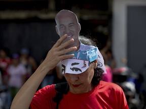 In this Oct 9, 2017 photo, a supporter of ruling party candidate Hector Rodriguez, who is running for governor of Miranda state, adjusts her hat featuring the 35-year-old candidate during a rally in Caracas, Venezuela. Candidates like Rodriguez, the young and charismatic rival to the opposition, have been waging their own get-out-the vote efforts and trying to appeal to a broader audience, ahead of Oct. 15 regional elections. (AP Photo/Fernando Llano)