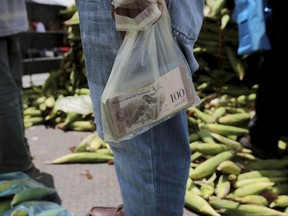 In this Sept. 23, 2017 photo, a vendor holds the bank notes in a plastic bag, at a market in Caracas, Venezuela. Venezuelans already struggling to find food, medicine and other basic necessities have a new headache to worry about: shortages of cash. Troubling shortfalls of Venezuelan bolivars are forcing many in this distressed South American nation to gather in long lines outside banks to take out what little cash is available.  (AP Photo/Fernando Llano)