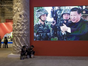 In this Thursday, Oct. 19, 2017, photo, video showing Chinese President Xi Jinping handling an assault rifle is shown at an exhibition highlighting China's achievements under five years of his leadership at the Beijing Exhibition Hall in Beijing. Xi is channeling a red-blooded nationalism as he seeks to strengthen the Communist Party's role in Chinese life and assert Beijing's rise as a global superpower. Xi's muscular foreign policy could become even more assertive following this month's party congress, where he's expected to get a second five-year term as party secretary general. (AP Photo/Ng Han Guan)