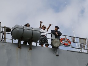 Jennifer Appel, center, raises her arms from bridge way of the USS Ashland Monday, Oct. 30 at White Beach Naval Facility in Okinawa, Japan. At left is Tasha Fuiava, and at right the Ashland's Command Master Chief Gary Wise. The U.S. Navy ship arrived at the American Navy base, five days after it picked up the women and their two dogs from their storm-damaged sailboat, 900 miles southeast of Japan. (AP Photo/Koji Ueda)