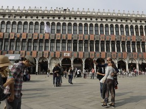 Tourists walk in front of the Procuratie Vecchie building, during the media launch of the restoration of the buildings and the Royal Gardens in St Mark's square in Venice, Italy, Wednesday, Oct. 4, 2017. British architect David Chipperfield is bringing his expertise in restoring historic buildings to the 500-year-old Procuratie Vecchie building on the northern edge of St. Mark's Square, which will house a new initiative to help disadvantaged people around the globe. (AP Photo/Luca Bruno)