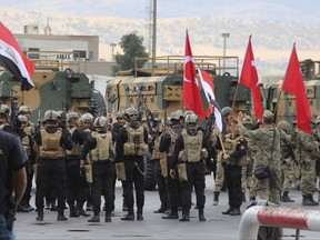 Turkish and Iraqi troops, some holding their national flags, participate in a ceremony at the Habur/Ibrahim Khalil border crossing with Iraq, near Silopi, southeastern Turkey, Tuesday, Oct. 31, 2017. Turkey's Prime Minister Binali Yildirim, in a speech, said that the border crossing was handed over to authorities of the Iraqi central government this morning. An Iraqi Kurdish official is denying reports that Iraqi federal forces have taken control of the key border crossing between Turkey and Iraq's northern Kurdish region that's in a major dispute with Baghdad. Border crossings have become a contested issue after last month's Kurdish independence referendum. (DHA-Depo Photos via AP)
