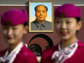 Hospitality staff members pose for a group photo near the large portrait of Mao Zedong on Tiananmen Gate before the closing ceremony of China's 19th Party Congress at the Great Hall of the People in Beijing, Tuesday, Oct. 24, 2017. The ruling Communist Party on Tuesday formally lifted Xi Jinping's status to China's most powerful ruler in decades, setting the stage for the authoritarian leader to tighten his grip over the country while pursuing an increasingly muscular foreign policy and military expansion. (AP Photo/Mark Schiefelbein)