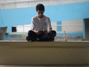 In this Friday, Oct. 13, 2017 photo, a youth sits in the courtyard of Ramon Marin Sola Elementary School, which opened its doors as a daytime community center after the passing of Hurricane Maria in Guaynabo, Puerto Rico, Most schools remain closed, leaving kids to pass the time playing on downed trees or using precious phone battery on video games, waiting for life to return to normal as the adults around them struggle to put their own lives back together. (AP Photo/Carlos Giusti)