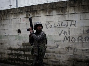 FILE - In this Aug. 21, 2017 file photo, a soldier takes position during a security operation next to a wall spray painted with a message that reads in Portuguese: "Police die," in the Jacarezinho slum, in Rio de Janeiro, Brazil. Thousands of soldiers and police are occupying a series of slum communities in northern part of the city as part of efforts to combat a spike in violence. (AP Photo/Silvia Izquierdo, File)