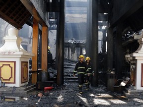 Firefighters walk at a burnt building following a fire at the Kandawgyi Palace Hotel Thursday, Oct. 19, 2017, in Yangon, Myanmar. A fire has nearly destroyed the luxury teakwood hotel popular with foreigners in Myanmar's biggest city of Yangon. (AP Photo/Thein Zaw)