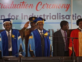 Zimbabwe's President Robert Mugabe, center, stands for the national anthem after arriving to preside over a student graduation ceremony at Zimbabwe Open University on the outskirts of Harare, Zimbabwe Friday, Nov. 17, 2017. Mugabe is making his first public appearance since the military put him under house arrest earlier this week. (AP Photo/Ben Curtis)