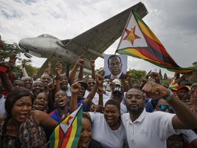 Supporters of Emmerson Mnangagwa, the man expected to become Zimbabwe's new president, hold a photograph of him and cheer as they arrive to show their support at Manyame Air Force base where Mnangagwa is expected to arrive later in the day in Harare, Zimbabwe Wednesday, Nov. 22, 2017. Mugabe resigned as president with immediate effect Tuesday after 37 years in power, shortly after parliament began impeachment proceedings against him. (AP Photo/Ben Curtis)