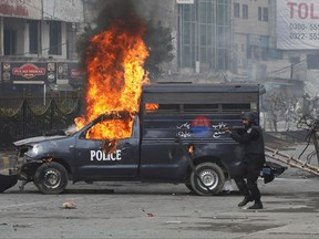 A Pakistani police officer aims his gun towards the protesters next to a burning police vehicle during a clash in Islamabad, Pakistan, Saturday, Nov. 25, 2017. Pakistani police have launched an operation to clear an intersection linking capital Islamabad with the garrison city of Rawalpindi where an Islamist group's supporters have camped out for the last 20 days. (AP Photo/Anjum Naveed)