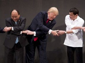 In this Monday, Nov. 13, 2017, file photo, U.S. President Donald Trump, center, reacts as he does the "ASEAN-way handshake" with Vietnamese Prime Minister Nguyen Xuan Phuc, left, and Philippine President Rodrigo Duterte on stage during the opening ceremony at the ASEAN Summit at the Cultural Center of the Philippines, in Manila. Trump initially did the handshake incorrectly. (AP Photo/Andrew Harnik, File)