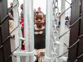 A girl who crossed the Canada/U.S. border illegally with her family, claiming refugee status, looks through a fence at a temporary detention centre in Blackpool, Que., on Aug. 5, 2017.