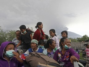 Villagers sit on a truck during an evacuation following the eruption of Mount Agung, seen in the background, in Karangasem, Indonesia, Sunday, Nov. 26, 2017.