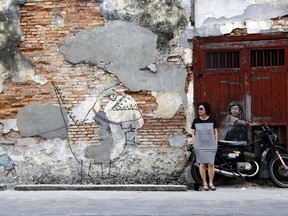 In this Saturday, Nov. 11, 2017, photo, a woman leans against a motorcycle incorporated into a street art installation by artist Ernest Zacharevic in George Town on the island of Penang, Malaysia. George Town oozes a hauntingly rustic charm, with colorful street art as much a draw as the historical architecture and one of Southeast Asia's tastiest street food scenes. (AP Photo/Adam Schreck)