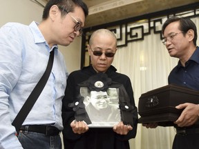 FILE - In this Saturday, July 15, 2017, file photo provided by the Shenyang Municipal Information Office, Liu Xia, center, wife of jailed Nobel Peace Prize winner and Chinese dissident Liu Xiaobo, holds a portrait of him during his funeral in Shenyang in northeastern China's Liaoning Province. Ahead of President Donald Trump's visit to Beijing, literary luminaries such as Margaret Atwood and Philip Roth are calling on China to free the widow of Nobel Peace Prize winner Liu Xiaobo. Also pictured are, from left to right, Liu Hui, younger brother of Liu Xia, Liu Xia and Liu Xiaoxuan, younger brother of Liu Xiaobo holding his cremated remains. (Shenyang Municipal Information Office via AP, File)