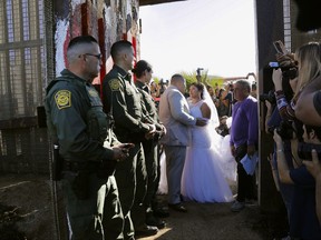 In this Saturday, Nov. 18, 2017, photo, Brian Houston, of Rancho San Diego, center left, and Evelia Reyes, right, of Tijuana, Mexico, look at each other in their wedding at the "Door of Hope," part of the border fence between the U.S. and Mexico. The United States man and the Mexican woman wedded Saturday between the doors of a steel border gate that opens for only an hour or so every year. Their wedding in San Diego was the first for an opening of the gate known as the Door of Hope. (Howard Lipin//The San Diego Union-Tribune via AP)