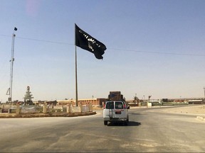 FILE - This Tuesday, July 22, 2014 file photo shows a motorist passing by a flag of the Islamic State group in central Rawah, 175 miles (281 kilometers) northwest of Baghdad, Iraq. Iraq's Defense Ministry said Friday, Nov. 17, 2017 Iraqi forces have retaken the last IS-held town in the country, more than three years after the militant group stormed nearly a third of Iraqi territory.(AP Photo, File)