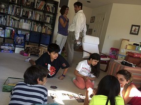 In this Friday, Oct. 27, 2017 photo, Lucia Cascio, top left, talks with her husband Raj Sodhi as their daughter Cascio, bottom in yellow, and son Jaco, bottom in black, play a game with friends at a friend's home in Santa Rosa, Calif. Cascio and Sodhi lost their home in Santa Rosa's Fountaingrove neighborhood in the wildfires. (AP Photo/Sudhin Thanawala)