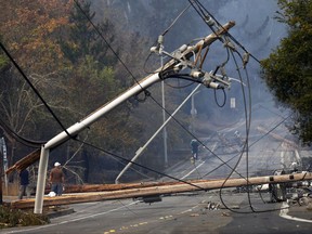 FILE - In this Tuesday, Oct. 10, 2017 file photo, people walk past a fallen transformer and downed power lines on Parker Hill Road in Santa Rosa, Calif. The wildfires that damaged much of remote Northern California areas, crippling cell phones, landlines and internet leads some to believe that old-fashioned sirens and ham radios might be more reliable in a disaster. (Nhat V. Meyer/San Jose Mercury News via AP, File)