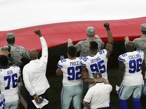 A member of the staff and Dallas Cowboys defensive tackle David Irving (95) throw up a fist just after the playing of the national anthem as members of the armed services hold an American flag before the first half of an NFL football game against the Kansas City Chiefs on Sunday, Nov. 5, 2017, in Arlington, Texas. (AP Photo/Roger Steinman)