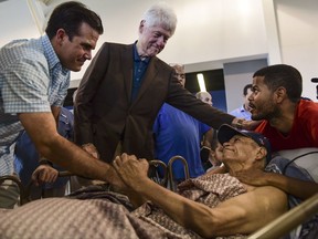 Former President Bill Clinton, top center, and Puerto Rico Governor Ricardo Rossello, left, greet Luis Andrew Torres Carrasquillo, right, and his father, a war veteran, Luis Torres Alemar, laying down, at the William Rivera Betancourt Vocational School which has been turned into an emergency shelter for families affected by the impact of Hurricane Maria, in Canovanas, Puerto Rico, Monday, Nov. 20, 2017.  (AP Photo/Carlos Giusti)