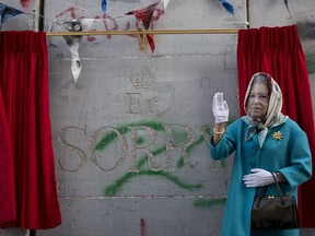 A woman wearing a mask of Queen Elisabeth stands next to the message by the elusive artist Banksy on the anniversary of the Balfour Declaration Bethlehem, West Bank, Wednesday, Nov. 1, 2017. The Balfour Declaration, Britain's promise to Zionists to create a Jewish home in what is now Israel, turns 100 this week, with events in Israel, the Palestinian territories and Britain drawing attention to the now yellowing document tucked away in London's British Library (AP Photo/Dusan Vranic)