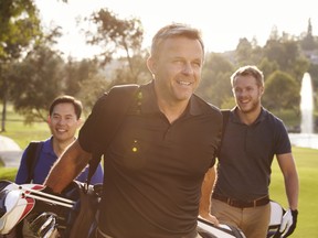 Group Of Male Golfers Walking Along Fairway Carrying Bags