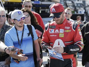 Dale Earnhardt Jr., right, gives autographs in the garage area during practice for Sunday's NASCAR Cup Series auto race at Homestead-Miami Speedway in Homestead, Fla., Friday, Nov. 17, 2017. (AP Photo/Terry Renna)