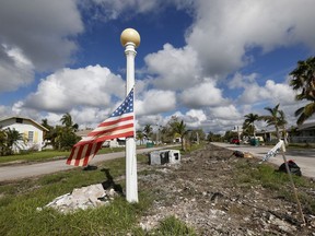In this Thursday, Nov. 9, 2017 photo, an American flag waves in the median where small piles of debris leftover from Hurricane Irma dot the landscape of a residential street, in Everglades City, Fla. Two months after Hurricane Irma's storm surge slammed through tiny Everglades City, the mountains of debris that lined the streets have been reduced to scattered piles and the occasional abandoned stove or refrigerator. (AP Photo/Wilfredo Lee)