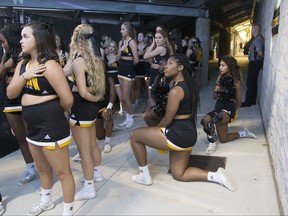 FILE - In this Saturday, Oct. 21, 2017, file photo, Four of the five Kennesaw State cheerleaders who took a knee three weeks ago during the Kennesaw State football game, take a knee once again out of sight of the fans under the visitors' bleachers, during the national anthem before an NCAA college football game between Kennesaw State and Gardner-Webb in Kennesaw, Ga. Kennesaw State, which moved its football cheerleaders inside a stadium tunnel after a group of black cheer squad members knelt during the national anthem, has decided to let them again take the field during pre-game ceremonies. (Kelly J. Huff/The Marietta Daily Journal via AP, File)