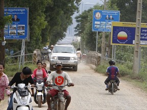 In this Oct. 23, 2017, photo, people travel past the signboard logos of the opposition Cambodia Rescue Party, CNRP, upper right, and Cambodian People's Party, upper left, placed on the roadside outside of Phnom Penh, Cambodia. A Cambodian opposition leader said Wednesday that he expects his political party to be dissolved in a Supreme Court ruling this week, a move that would further descend the nation into authoritarianism ahead of next year's general election. (AP Photo/Heng Sinith)