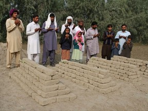 Relatives of poisoning victims pray at their graves in Basti Lashari, Pakistan, Wednesday, Nov. 8, 2017. Pakistani police arrested a woman for allegedly plotting with her newly married niece to poison the niece's husband with tainted milk that also ended up killing 17 other in-laws in a remote village. (AP Photo/Iram Asim)