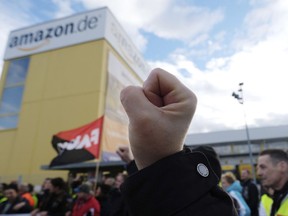 A participant of a demonstration raises his fist in front of the local site of the online retail company Amazon in Leipzig, Germany, Friday, Nov. 24 2017. A labor union says workers at a half dozen Amazon distribution centers in Germany have walked off the job, the latest in a string of walkouts in a long-running wage dispute with the American online retailer at one of its busiest times. (Sebastian Willnow/dpa via AP)