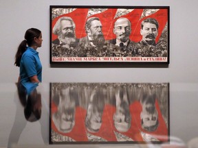 A visitor looks towards Lithographs on paper from 1933 called 'Under the Banner of Marx, Engels, Lenin and Stalin!' on display at the Tate Modern in the Red Star Over Russia exhibition in London, Tuesday, Nov. 7, 2017. The exhibition is to mark the centenary of the October Revolution, it offers a visual history of Russia and the Soviet Union. (AP Photo/Kirsty Wigglesworth)