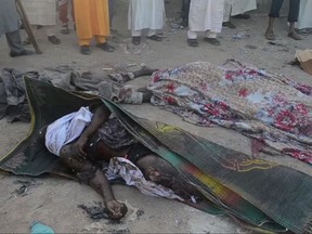 In this image taken from TV, people stand around dead bodies after a deadly attack by a suicide bomber at a mosque in Mubi, Adamawa State, Nigeria, Tuesday Nov. 21, 2017.  A teenage suicide bomber detonated as worshippers gathered for morning prayers at a mosque in northeastern Nigeria, killing at least 50 people, police said Tuesday, in one of the region's deadliest attacks in years. (AP Photo)