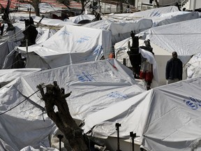 FILE - In this photo taken on Thursday, March 16, 2017, a migrant stands between tents at the Moria refugee detention center on the northeastern Greek island of Lesbos. Authorities on Lesbos have called a for residents to strike during anti-government protests to press for a change in the European Union policy of containment of refugees and migrants on the Greece's islands which have turned Lesbos into an "island prison", according to island authorities.(AP Photo/Thanassis Stavrakis, FILE)