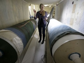 In this Tuesday, Nov. 7, 2017 photo textile conservator Kate Tarleton, of Rochester, Mass., stands between two oversized spools holding a portion of the 1848, "Grand Panorama of a Whaling Voyage Round the World," at the museum in New Bedford, Mass. The quarter-mile-long (0.4-kilometer-long) panorama toured the U.S. after it was completed in 1848. . (AP Photo/Steven Senne)