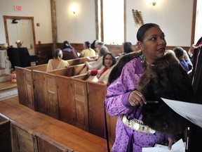 In this Saturday, Nov. 18, 2017, photo Toodie Coombs, of East Falmouth, Mass., right, distributes prayer pamphlets written in Wampanoag and English before the "We Gather Together" celebration at the Old Indian Meeting House, in Mashpee, Mass. The Mashpee Wampanoag tribe is in its second year of operating a preschool immersion program where only an indigenous language that had not been spoken for generations is uttered. The tribe also has launched language classes for high school students, tribal elders and tribal families. (AP Photo/Steven Senne)