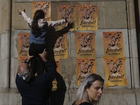 A girl pastes a banner on a wall that reads in Catalan: "Freedom for the Political Prisoners", during a protest against the decision of a judge to jail ex-members of the Catalan government at the University square in Barcelona, Spain, Sunday, Nov. 5, 2017. A Spanish judge issued an international arrest warrant on Friday for former members of the Catalan Cabinet who were last seen in Brussels, including the ousted separatist leader Carles Puigdemont, who said he was prepared to run for his old job even while battling extradition in Belgium. (AP Photo/Manu Fernandez)