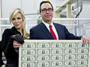 Treasury Secretary Steven Mnuchin, right, and wife, Louise Linton, hold an uncut sheet of $1 dollar notes. The new $1 bills, with Mnuchin and U.S. Treasurer Jovita Carranza's signatures, are expected to go into circulation in December.